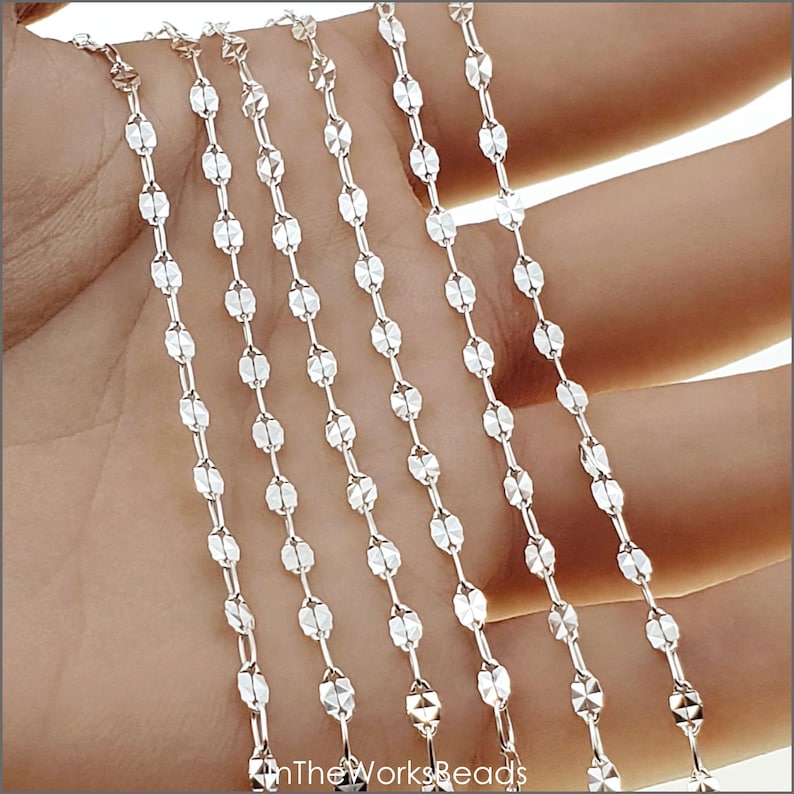 May include: Five strands of silver chain with a faceted oval link design. The chain is shown on a hand, with the ends of the chain hanging down.