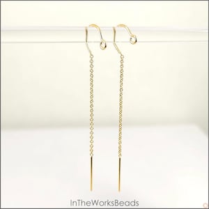 May include: A pair of gold-toned dangle earrings with a chain design and a straight, thin bar at the bottom.