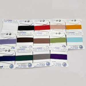 May include: Assortment of Nylon Power beading thread spools in various colors. Each spool is labeled with the brand name, thread size, and length. The spools are arranged in rows on a white background.