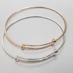 May include: Two expandable bangle bracelets, one silver and one gold, with a simple knot closure.