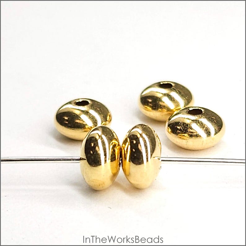 May include: Four gold-coloured metal beads, two of which are strung on a silver wire. The beads are round and have a smooth, shiny finish.