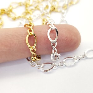 May include: Close-up of gold, silver, and gold-coloured chain links. The chains are oval-shaped and connected in a repeating pattern. The chains are displayed on a white background.