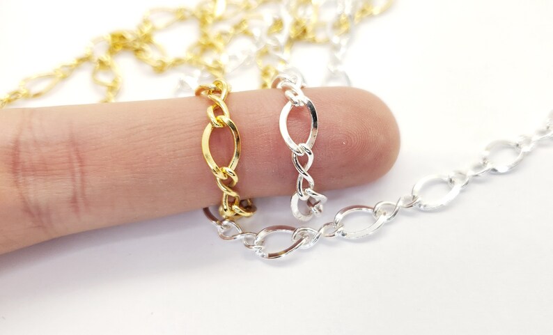 May include: Close-up of gold, silver, and gold-coloured chain links. The chains are oval-shaped and connected in a repeating pattern. The chains are displayed on a white background.
