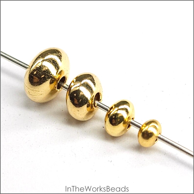 May include: Four gold-coloured metal beads of different sizes strung on a wire. The beads are round and have a smooth, shiny finish.