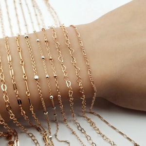 May include: A collection of gold chain bracelets with different link styles, including a coin chain, a cable chain, a curb chain, and a heart chain.