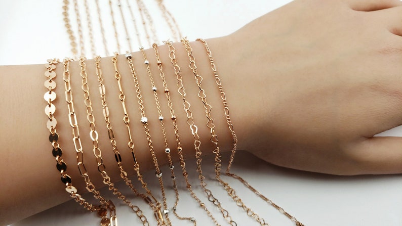 May include: A collection of gold chain bracelets with different link styles, including a coin chain, a cable chain, a curb chain, and a heart chain.