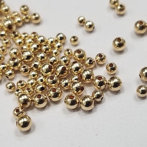 May include: A large quantity of small, round, gold-coloured beads. The beads are scattered on a white surface.