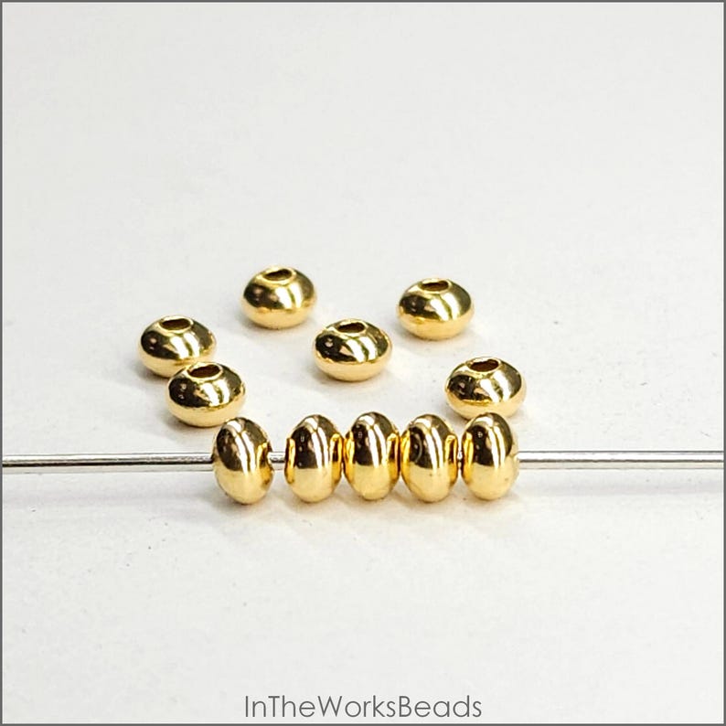May include: A close-up of a strand of gold-coloured beads, with additional beads scattered around. The beads are round and have a smooth, shiny finish.
