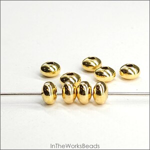 May include: Gold-coloured metal beads with a smooth, rounded surface. The beads are strung on a thin wire and are arranged in a row. There are also several loose beads scattered around the wire.