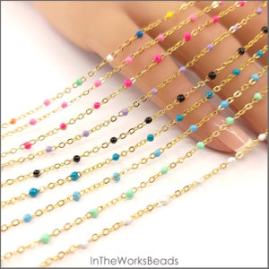 Puede incluir: Una variedad de cadenas doradas con pequeñas cuentas de colores. Las cadenas están dispuestas en forma de abanico en una mano. Las cuentas son de colores como blanco, negro, turquesa, rosa y verde.