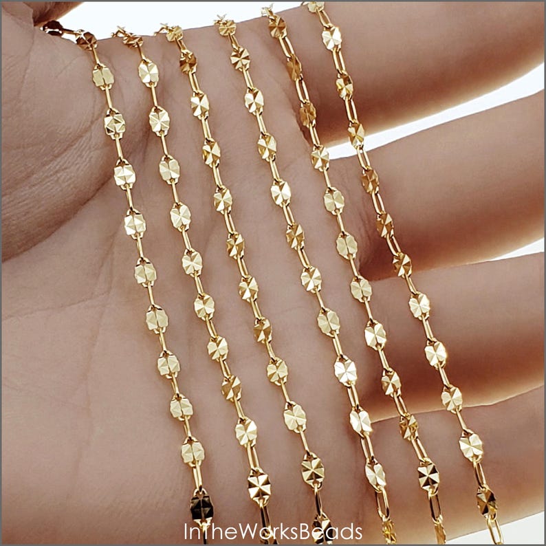 May include: Six strands of gold-toned chain with a faceted oval link design. The chain is displayed on a hand.