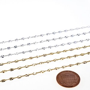 May include: Four rows of silver and gold chain, each with a different length. The chains are made of small, oval-shaped links with a faceted design. A US penny is included for scale.