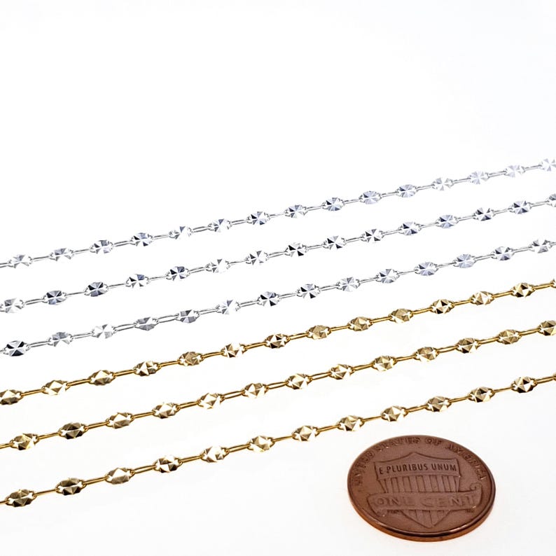 May include: Four rows of silver and gold chain, each with a different length. The chains are made of small, oval-shaped links with a faceted design. A US penny is included for scale.