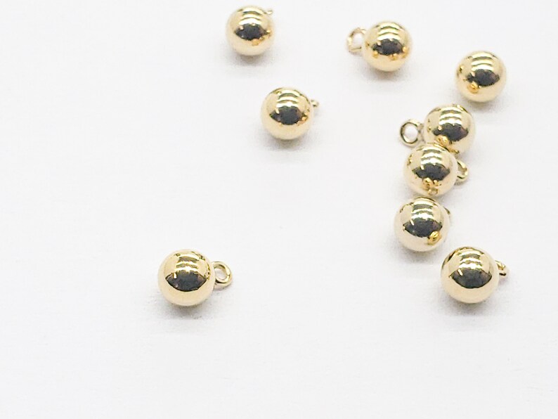May include: A group of ten gold-colored round buttons with a small loop on each button.