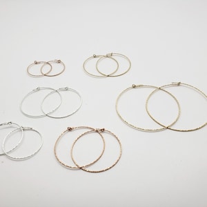 May include: A set of six hoop earrings in different sizes and colors. The earrings are made of silver, gold, and rose gold. They are all textured and have a slightly hammered finish.