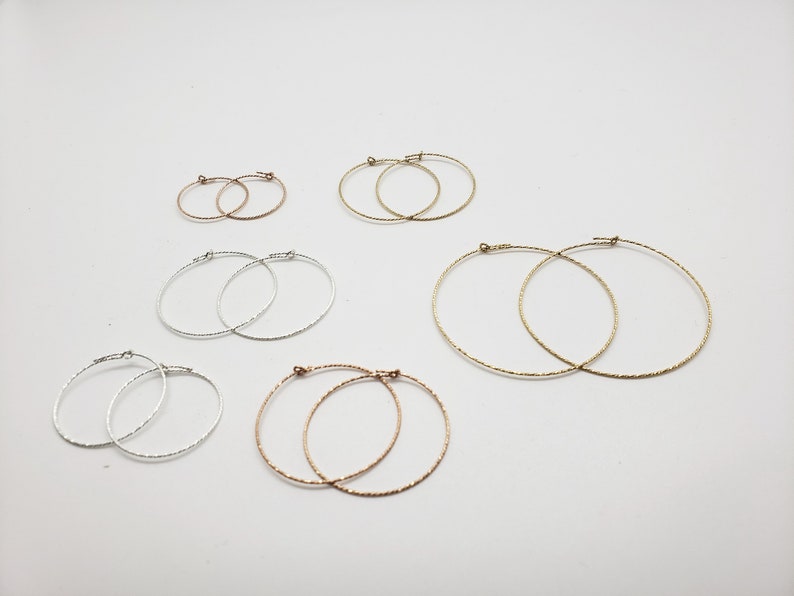 May include: A set of six hoop earrings in different sizes and colors. The earrings are made of silver, gold, and rose gold. They are all textured and have a slightly hammered finish.