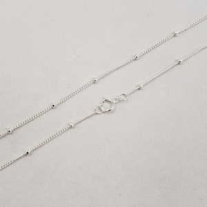 May include: A silver chain necklace with small round beads. The chain is delicate and has a lobster clasp.