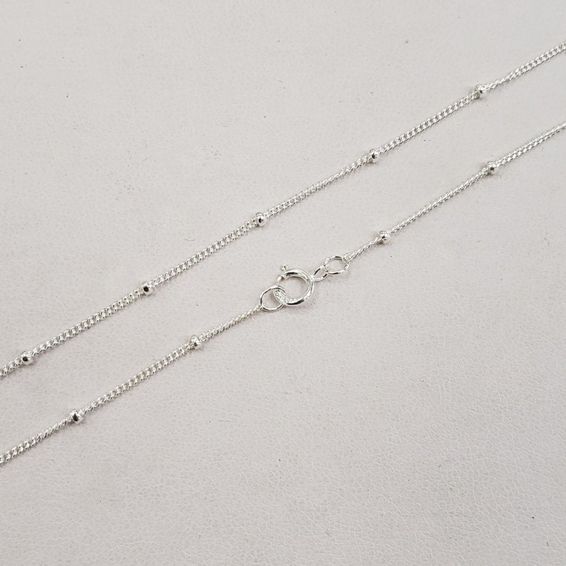 May include: A silver chain necklace with small round beads. The chain is delicate and has a lobster clasp.