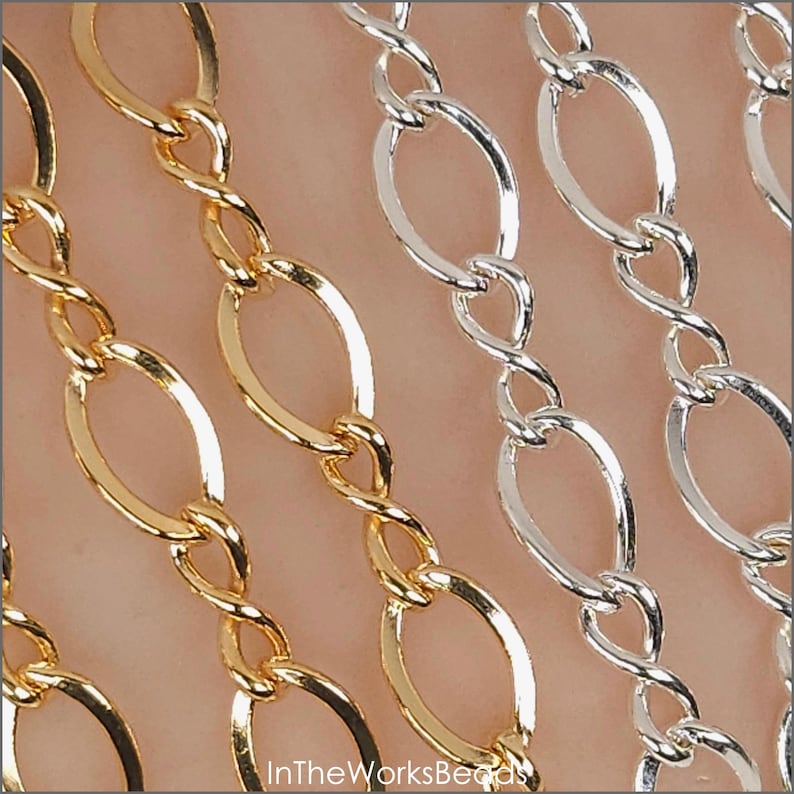 May include: Close-up of gold and silver oval link chains. The chains are arranged in parallel rows, with each link connected by a twisted bar. The gold chains are on the left, and the silver chains are on the right. The text "InTheWorksBeads" is at the bottom.