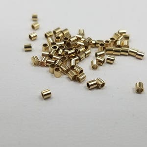 May include: A pile of gold-colored jump rings, also known as split rings, are scattered on a white surface. These rings are used for jewelry making and crafting.
