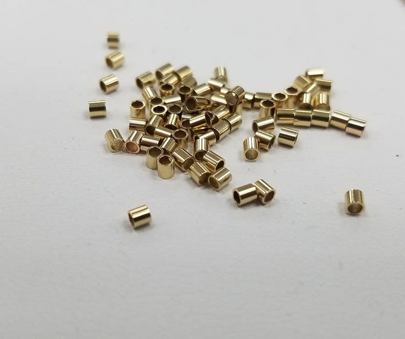 May include: A pile of gold-colored jump rings, also known as split rings, are scattered on a white surface. These rings are used for jewelry making and crafting.