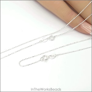 May include: Two silver chains with a lobster clasp closure. The chains are made of small, round beads.
