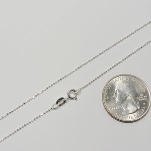 Puede incluir: Un collar de cadena de plata con cierre de langosta. La cadena mide aproximadamente 45 cm de largo y se muestra junto a una moneda de 25 centavos de d&oacute;lar estadounidense para comparar el tama&ntilde;o.