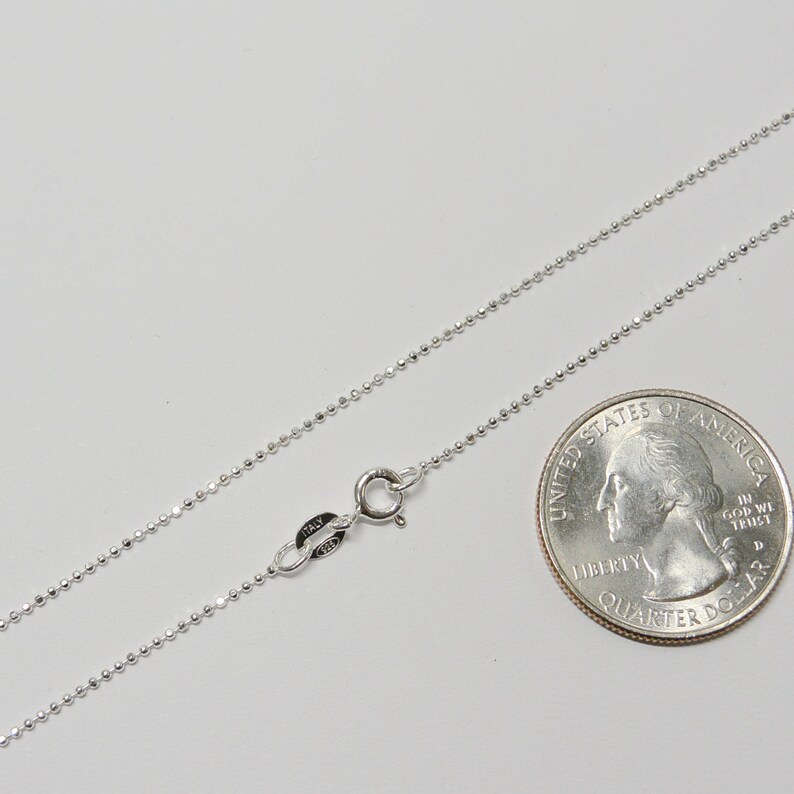 Puede incluir: Un collar de cadena de plata con cierre de langosta. La cadena mide aproximadamente 45 cm de largo y se muestra junto a una moneda de 25 centavos de d&oacute;lar estadounidense para comparar el tama&ntilde;o.
