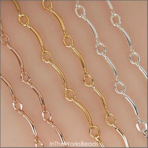 May include: Close-up of several delicate chain necklaces in gold, rose gold, and silver. Each chain features a series of curved bars connected by small circular links. The chains are displayed against a neutral background.