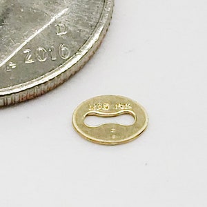 May include: A small, oval-shaped gold connector with a cutout in the center. The connector is marked with "14K" on the top and "14K" on the bottom.