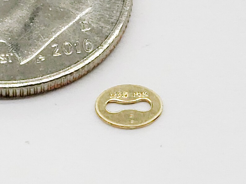 May include: A small, oval-shaped gold connector with a cutout in the center. The connector is marked with "14K" on the top and "14K" on the bottom.