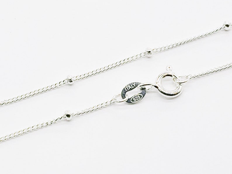 May include: A silver chain necklace with small round beads. The chain has a lobster clasp and a tag that reads "ITALY 925".