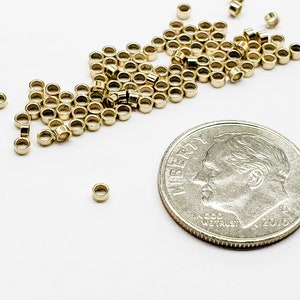 May include: A pile of gold jump rings, some of which are scattered around a US dime coin. The jump rings are small and round, and they are used for jewelry making.