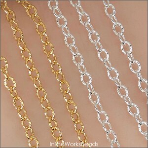 Könnte beinhalten: Nahaufnahme von mehreren Strängen gold- und silberfarbener Kette. Die Ketten bestehen aus kleinen, oval geformten Gliedern. Die Ketten sind diagonal über den Rahmen angeordnet und bilden ein Muster. Der Hintergrund ist neutral gefärbt.
