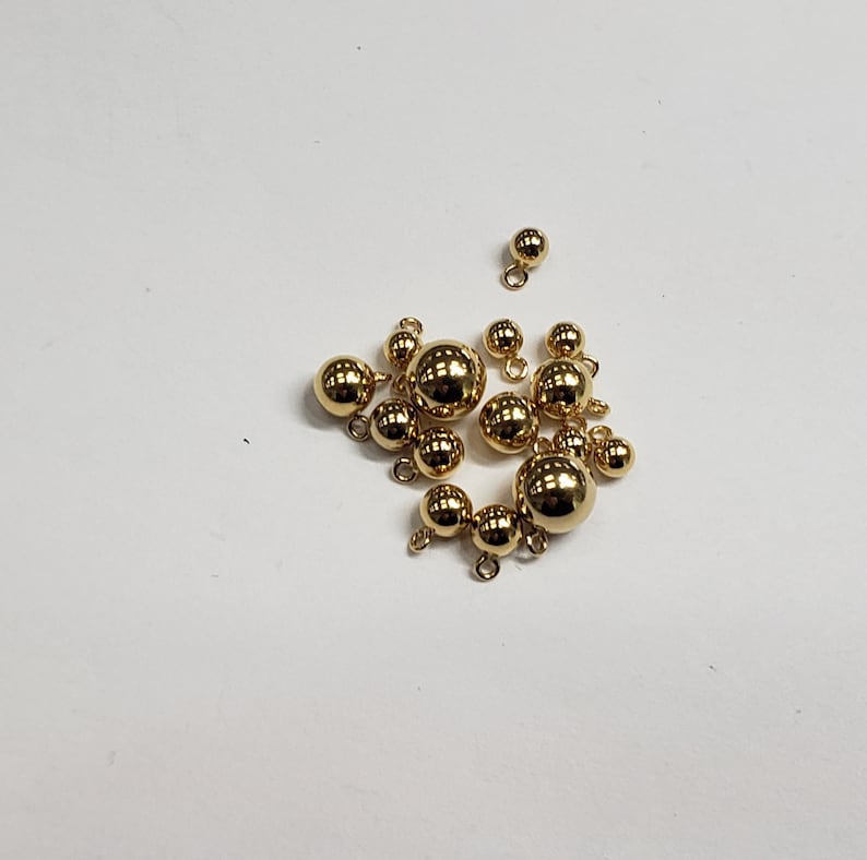 May include: A group of gold-colored metal beads with loops, some of the beads are larger than others.