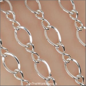 May include: Close-up of a silver chain featuring oval links and twisted connectors. The chain has a bright, reflective surface with a polished finish. The links are evenly spaced, forming a repeating pattern. The chain is suitable for jewellery or craft projects.