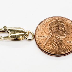 Puede incluir: Cierre de langosta dorado para la elaboraci&oacute;n de joyas, junto a un centavo de d&oacute;lar estadounidense para comparar el tama&ntilde;o.