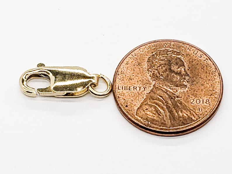 Puede incluir: Cierre de langosta dorado para la elaboraci&oacute;n de joyas, junto a un centavo de d&oacute;lar estadounidense para comparar el tama&ntilde;o.