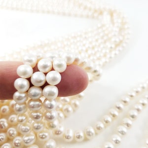 Peut inclure: Un collier de perles blanches, avec un gros plan sur une section des perles tenues dans une main.