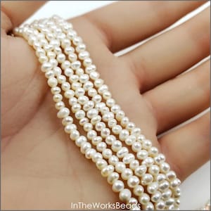 May include: A strand of small, off-white, irregularly shaped freshwater pearls with a lustrous finish. The pearls are strung together in a continuous line, displaying natural variations in size and texture. The text InTheWorksBeads is visible.
