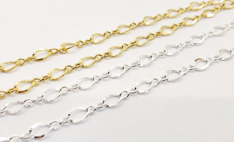 May include: Close-up of three delicate chains in gold and silver. The chains feature an oval link design, with two gold chains at the top and a silver chain below. The chains are displayed against a white background, showcasing their intricate details.
