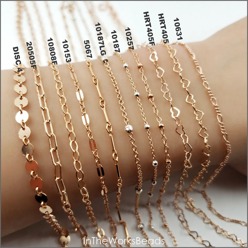 May include: A collection of 11 gold chain bracelets with different styles, including heart, bar, and round links. The bracelets are displayed on a person's wrist.