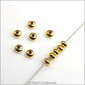 May include: Gold-coloured metal beads, some are loose and others are strung on a wire. The beads are round and have a slightly raised centre.