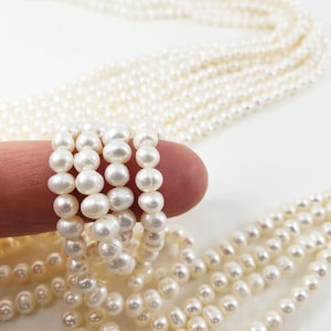 Peut inclure: Un brin de perles d'eau douce blanches, enroulé autour d'un doigt. Les perles sont rondes et lisses, avec un léger éclat.