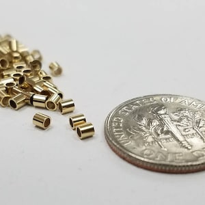 May include: A pile of small, gold-colored metal jump rings, some of which are scattered around the pile. A US dime is included for scale.