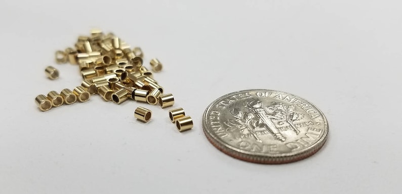 May include: A pile of small, gold-colored metal jump rings, some of which are scattered around the pile. A US dime is included for scale.