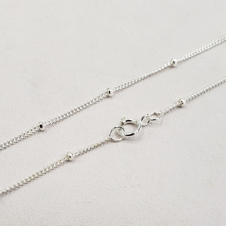 May include: A silver chain necklace with small round beads. The chain is delicate and has a lobster clasp.