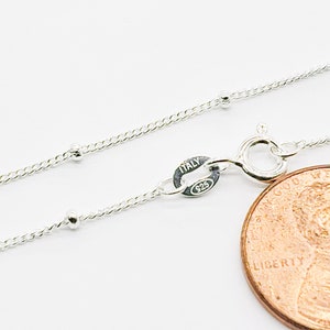 May include: A silver chain necklace with small round beads. The chain is shown next to a US penny for size comparison. The clasp is marked "Italy 925".