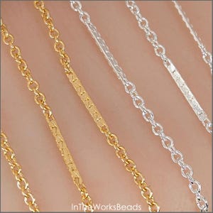 May include: Close-up of gold and silver-colored chain necklaces. The gold chains have a textured bar design, while the silver chains have a simple, classic design. The chains are displayed on a neutral background. The text "InTheWorksBeads" is visible.
