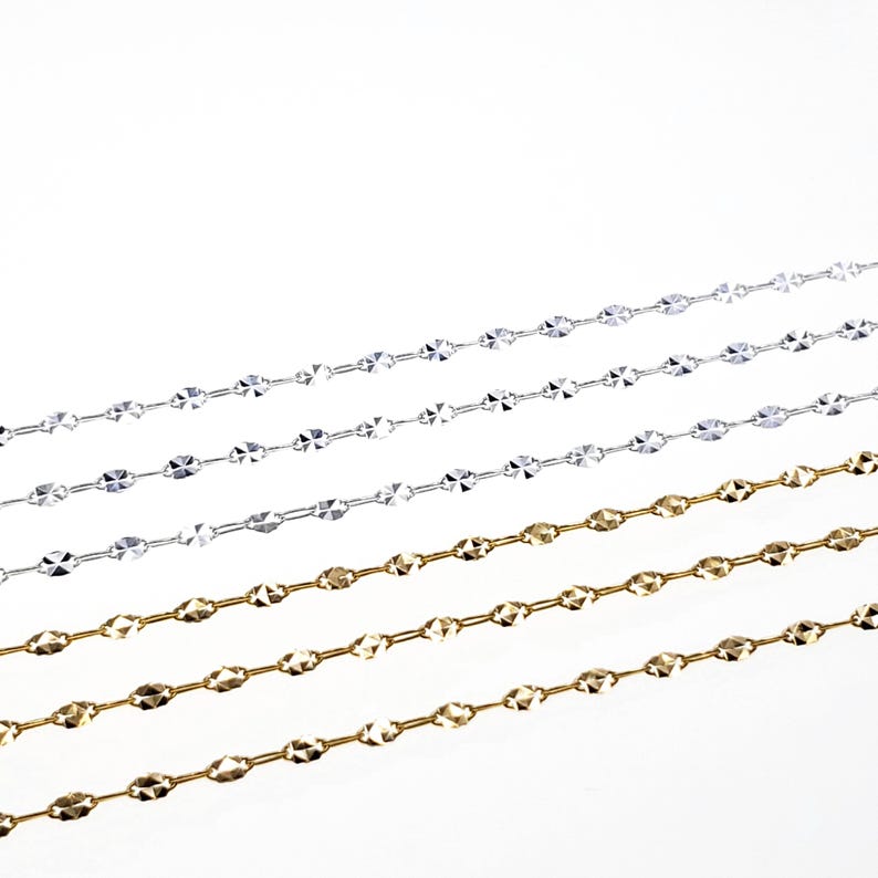 May include: Four chains, two silver and two gold, with a diamond-cut pattern. The chains are laid out in a diagonal pattern on a white background.